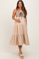 woman wearing a beige maternity dress with a smocked bodice and tiered skirt, holding her baby bump