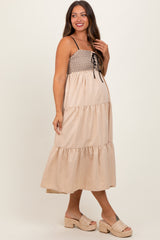 woman wearing a beige maternity dress with a lace-up bodice and tiered skirt, showcasing her baby bump