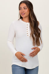 woman wearing a white ribbed long sleeve maternity top with ruffled neckline and button details, holding her baby bump