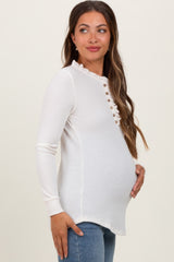 woman wearing a white long sleeve maternity top with ruffled neckline and button details, holding her baby bump