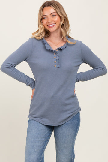 woman wearing a blue long sleeve henley top with a ruffled collar and button details, smiling with hands on hips