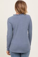 woman wearing a light blue long sleeve top with ruffle neckline and textured fabric, viewed from the back