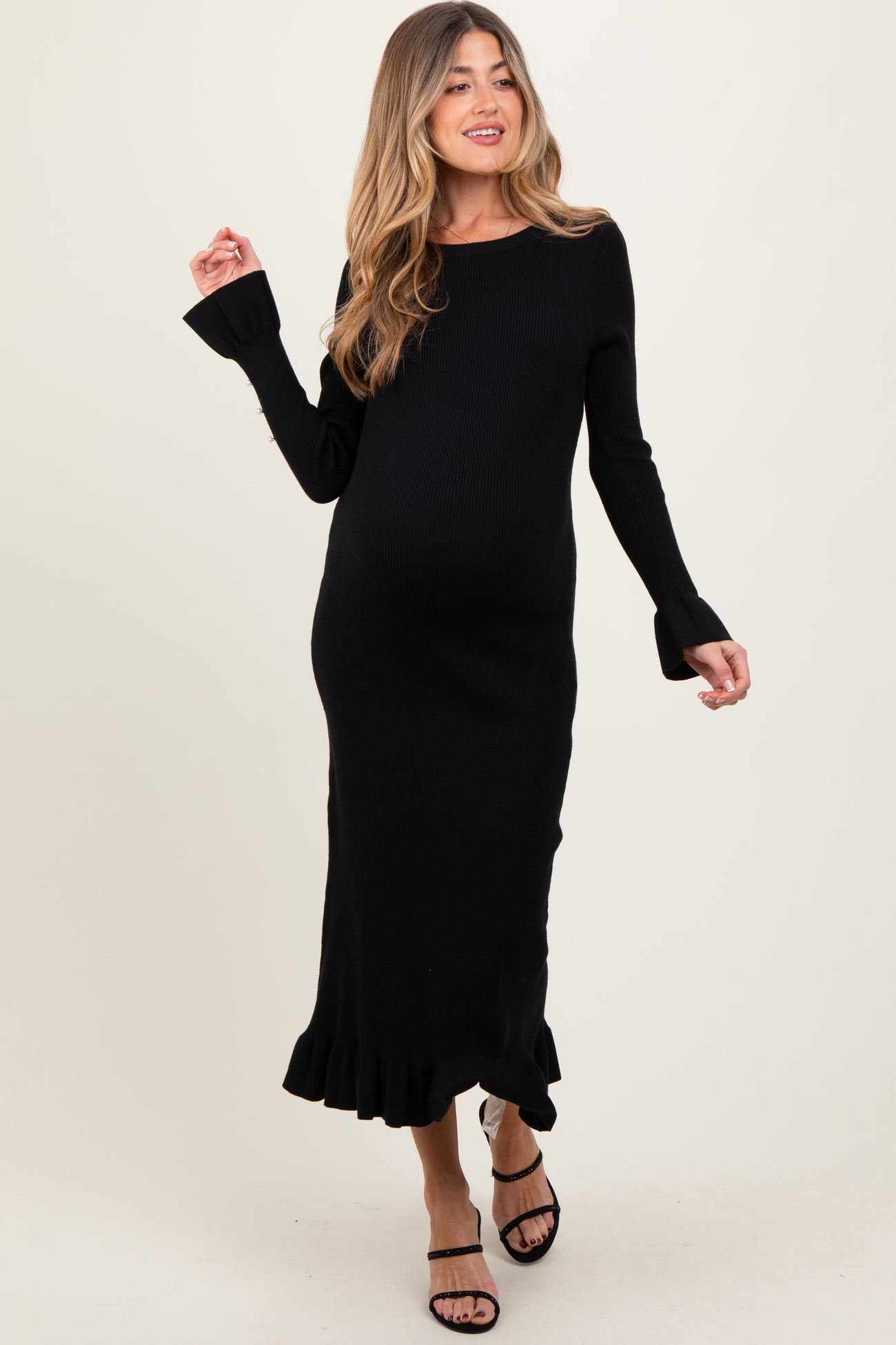 woman wearing a black ribbed maternity dress with ruffled hem and bell sleeves, showing her baby bump