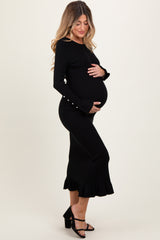 woman wearing a black ribbed maternity dress with bell sleeves and ruffle hem, cradling her baby bump