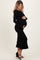 woman wearing a black ribbed maternity dress with bell sleeves and ruffle hem, cradling her baby bump