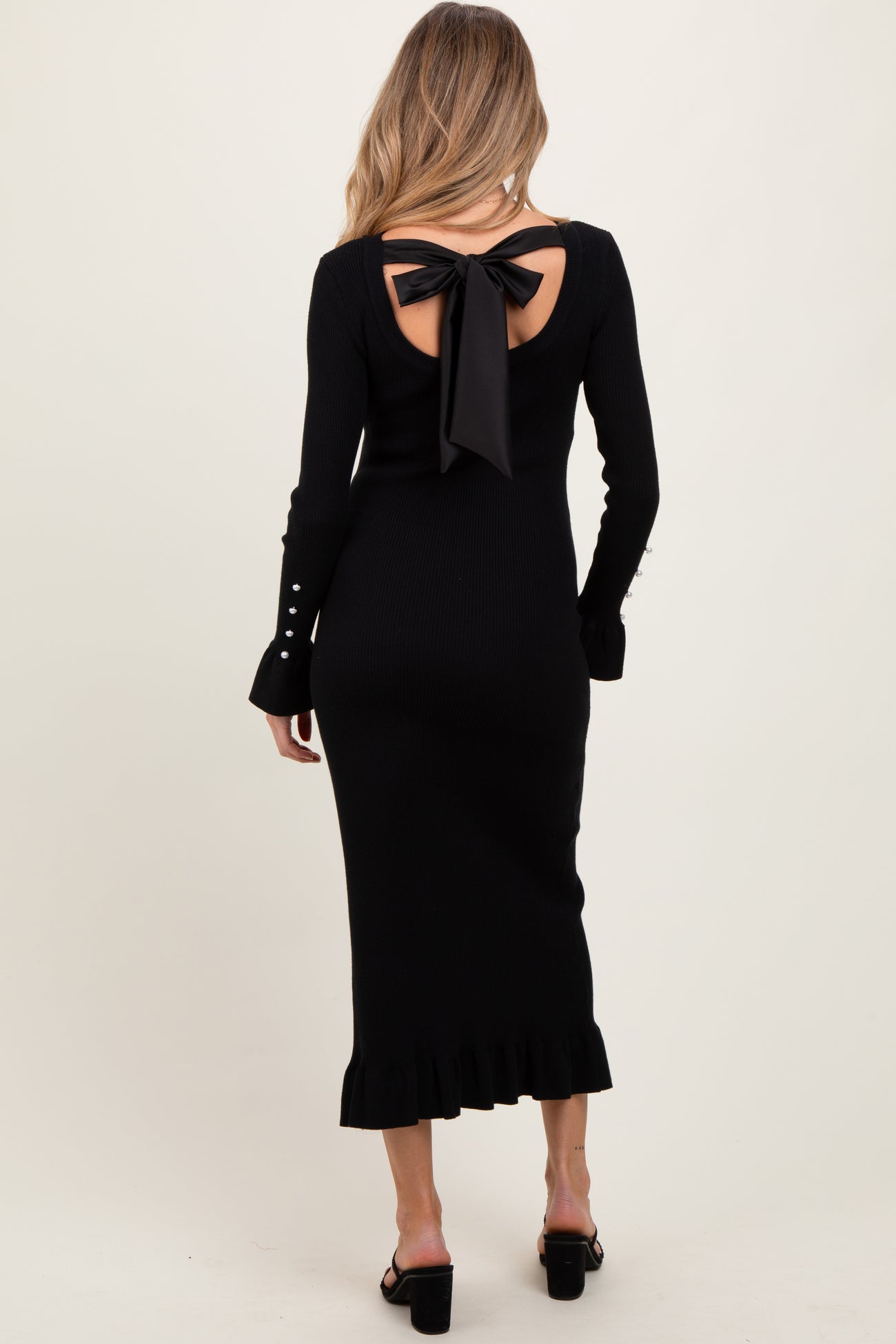 woman wearing a black ribbed maternity dress with a bow detail at the back and ruffle hem