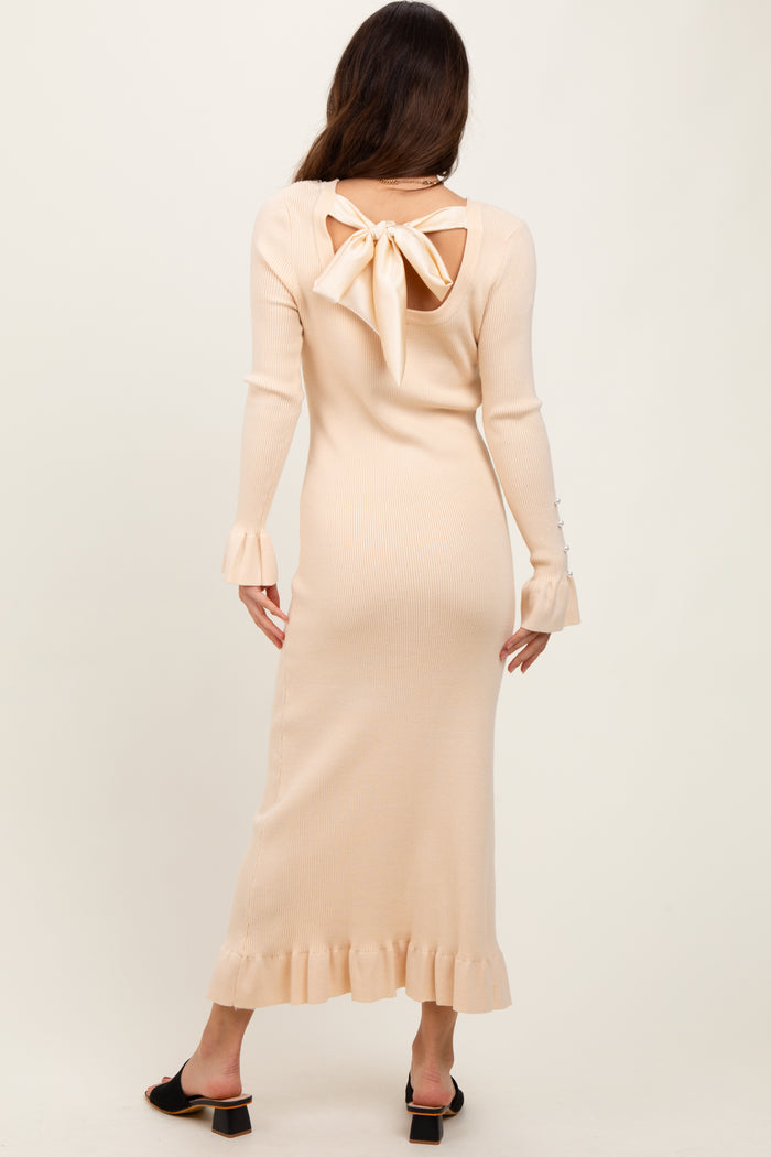 woman wearing a light peach ribbed midi dress with a back cutout and bow detail, featuring ruffled sleeves and hem
