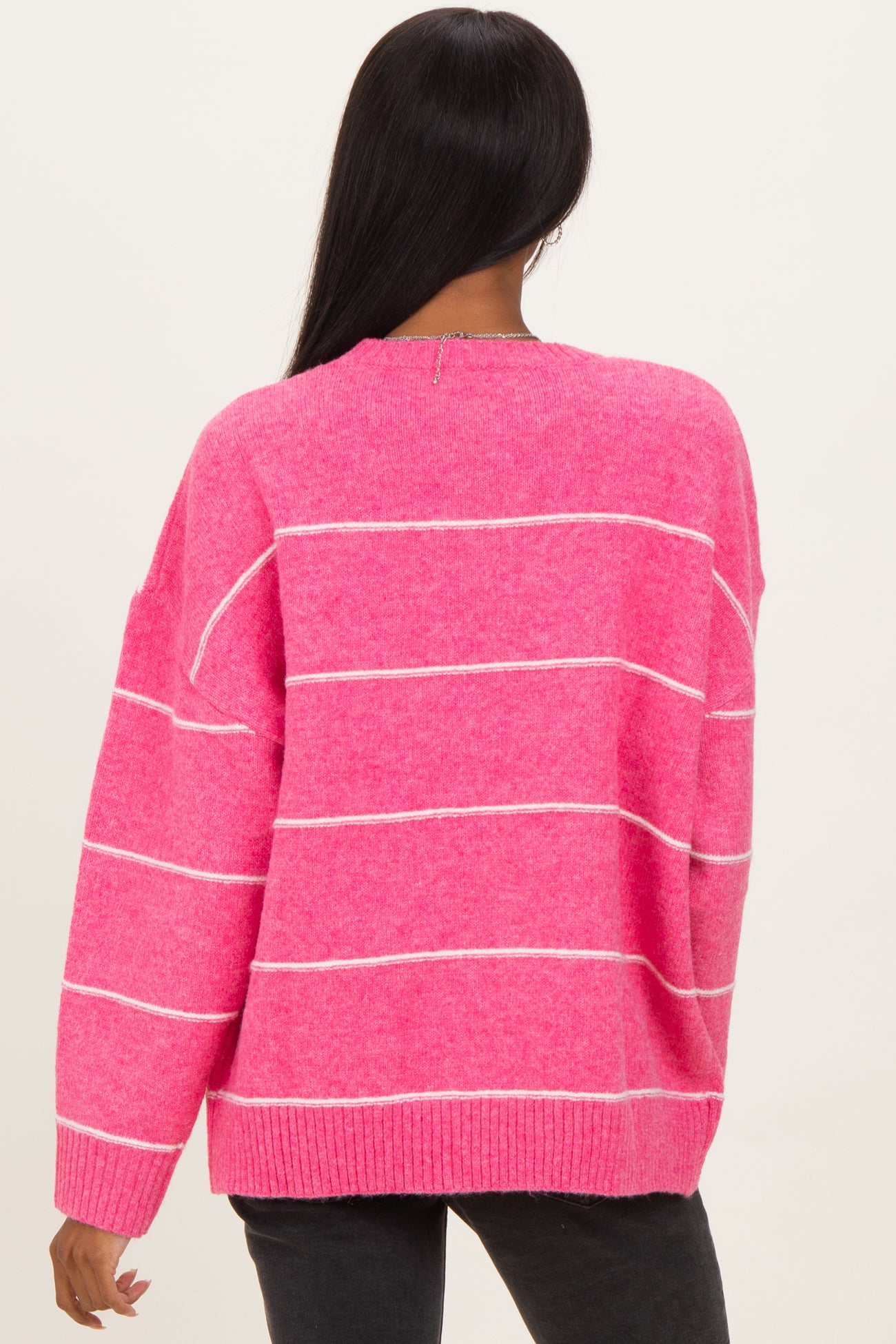 woman wearing a bright pink striped sweater with a relaxed fit, showing the back view and long sleeves