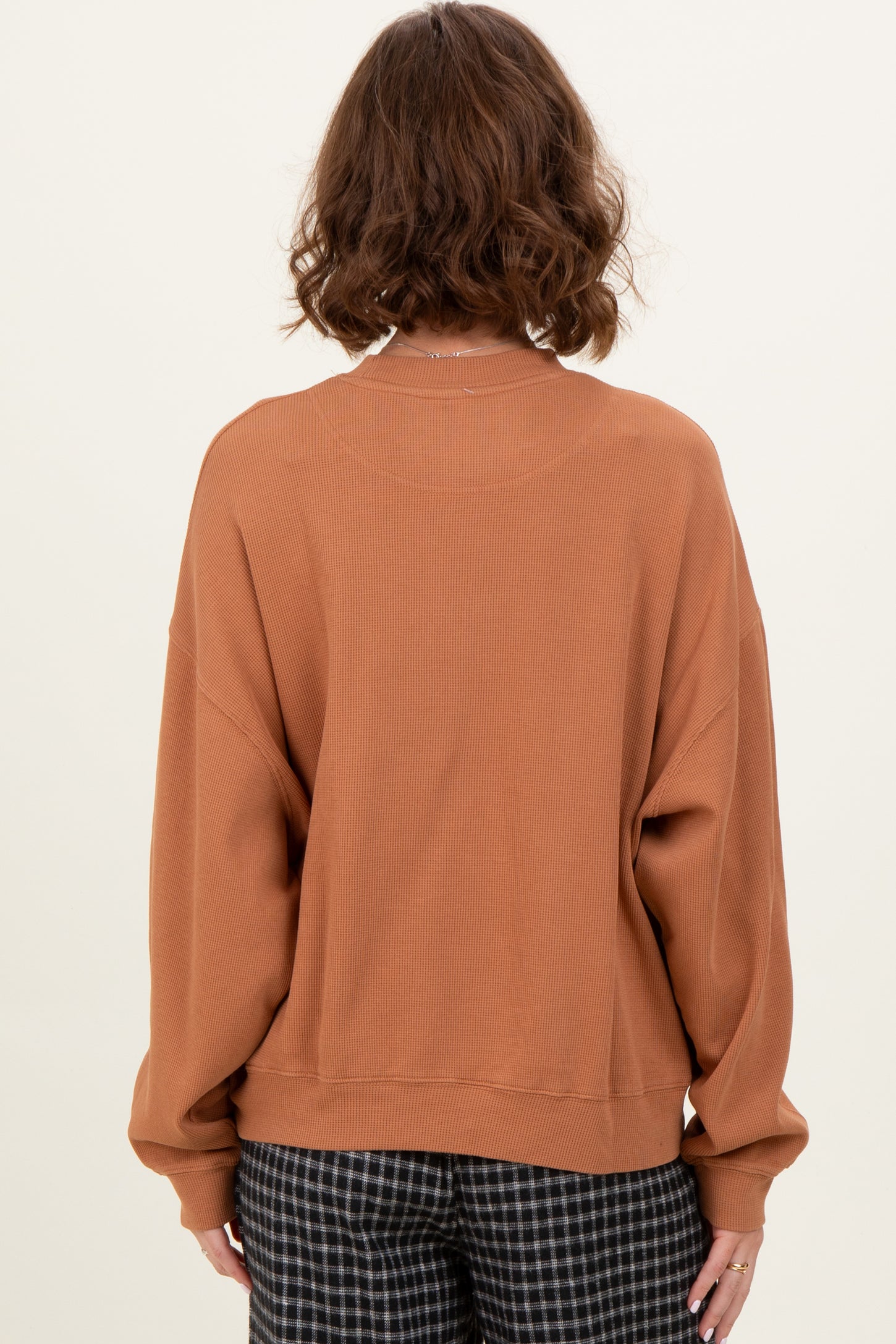 woman wearing a rust colored oversized sweater with long sleeves and a relaxed fit, viewed from the back