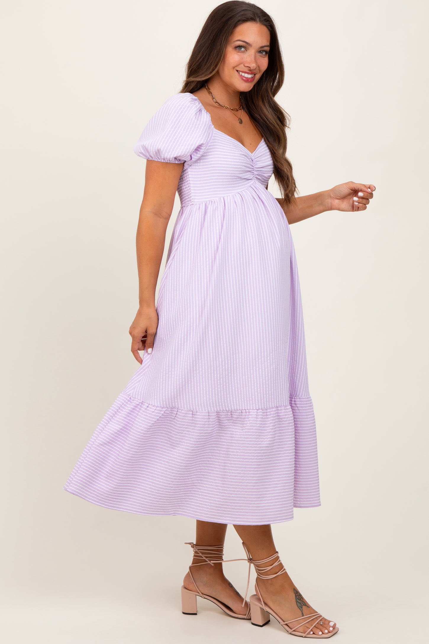 woman wearing a lavender striped maternity dress with puff sleeves and a ruffled hem, showcasing her baby bump
