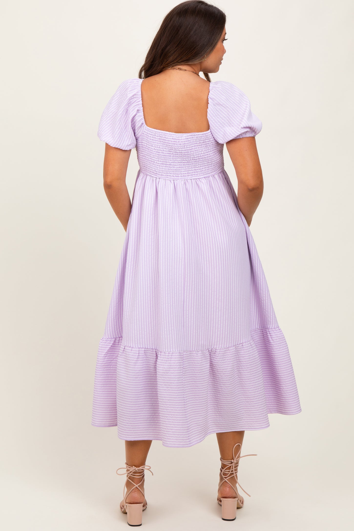 woman wearing a lilac striped maternity dress with puff sleeves and a tiered hem, showcasing her baby bump