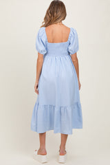woman wearing a light blue striped maternity dress with puff sleeves and a tiered hem, showing her back