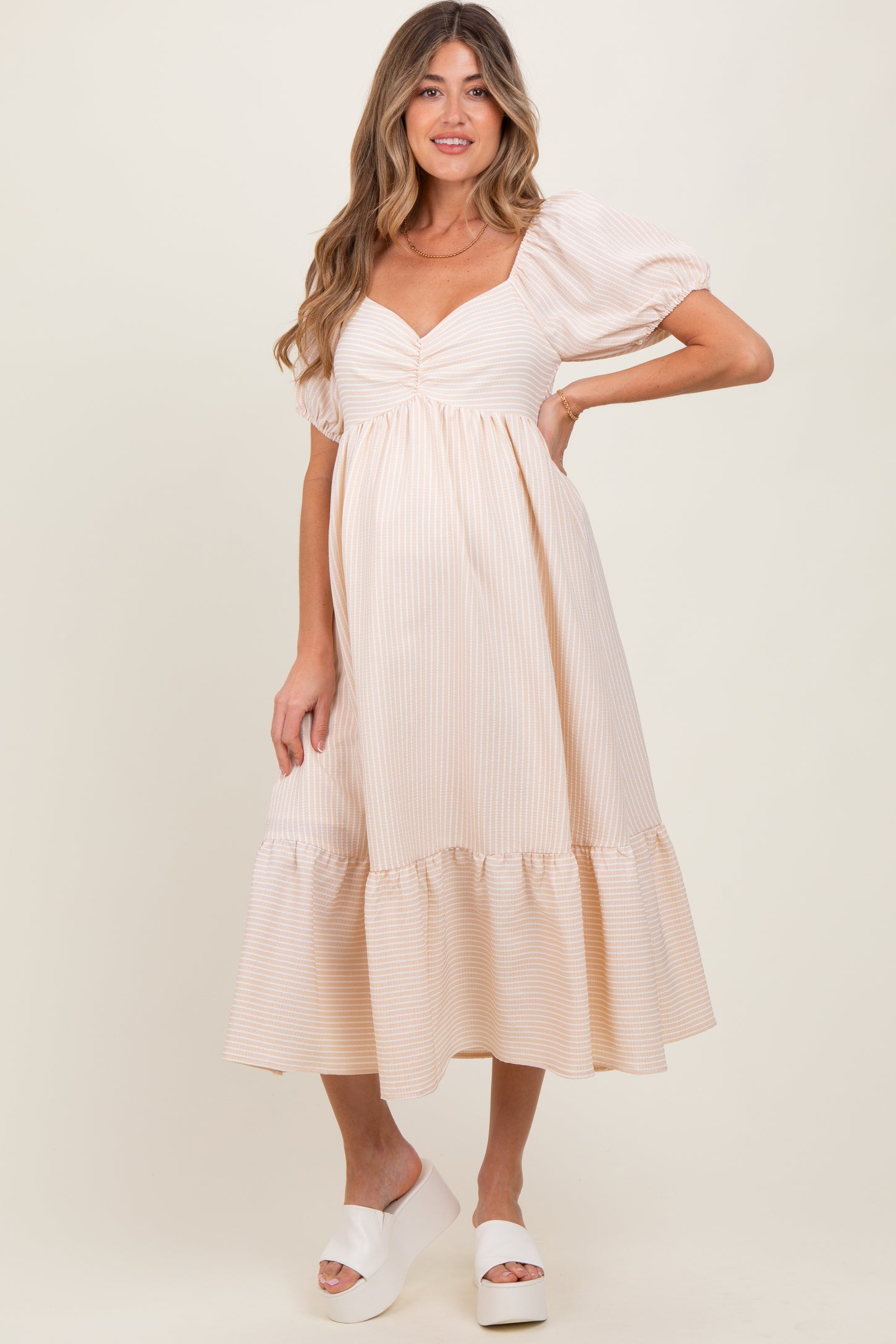 woman wearing a striped beige maternity dress with puff sleeves and a tiered hem, highlighting her baby bump