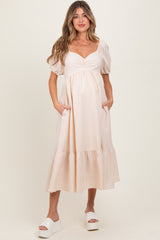 woman wearing a striped beige maternity dress with puff sleeves and pockets, standing and smiling