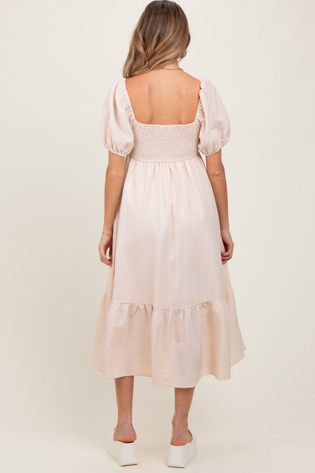 woman wearing a light pink striped maternity dress with puff sleeves and a smocked back, showing off a baby bump