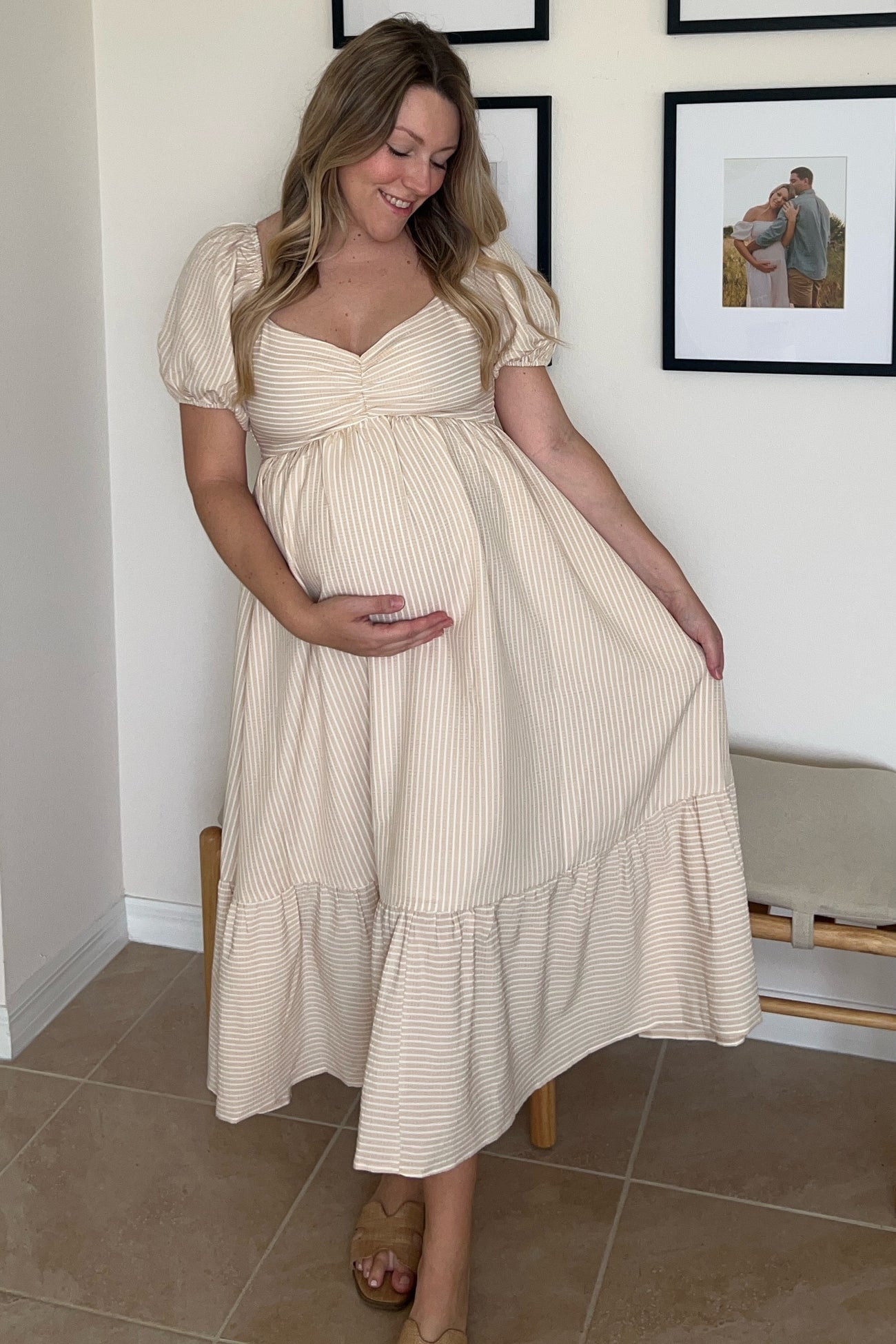 woman wearing a cream striped maternity dress with puff sleeves and a tiered skirt, holding her baby bump
