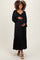 woman wearing a black maternity maxi dress with a bow detail and a ruffled hem, holding her baby bump