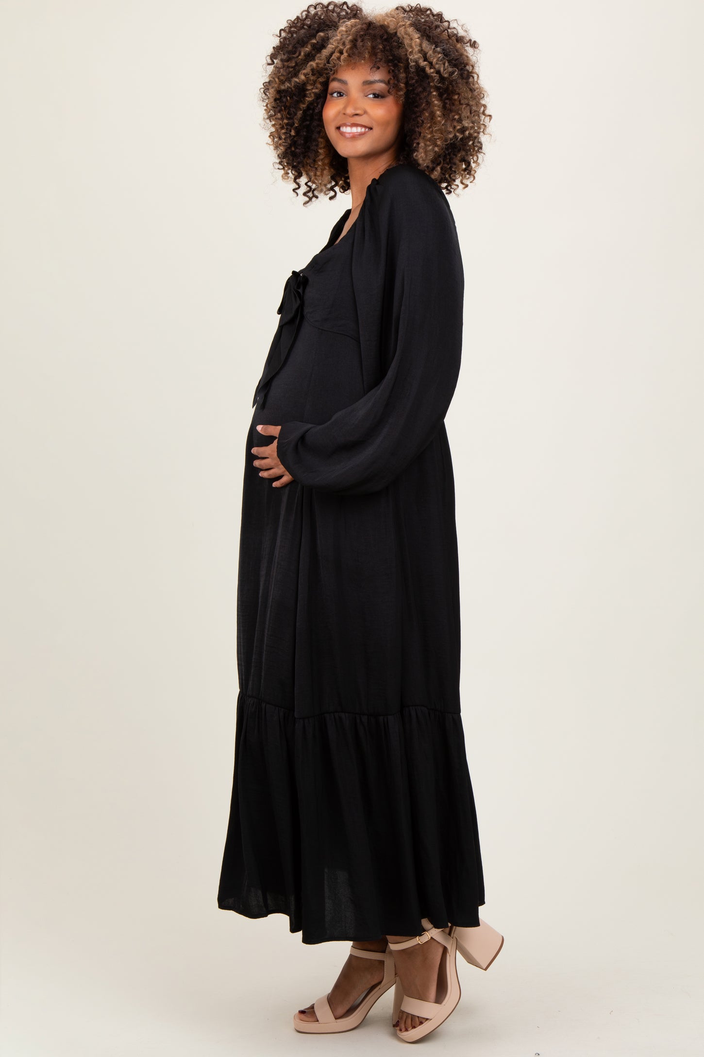 woman wearing a black maternity maxi dress with a bow detail and holding her baby bump