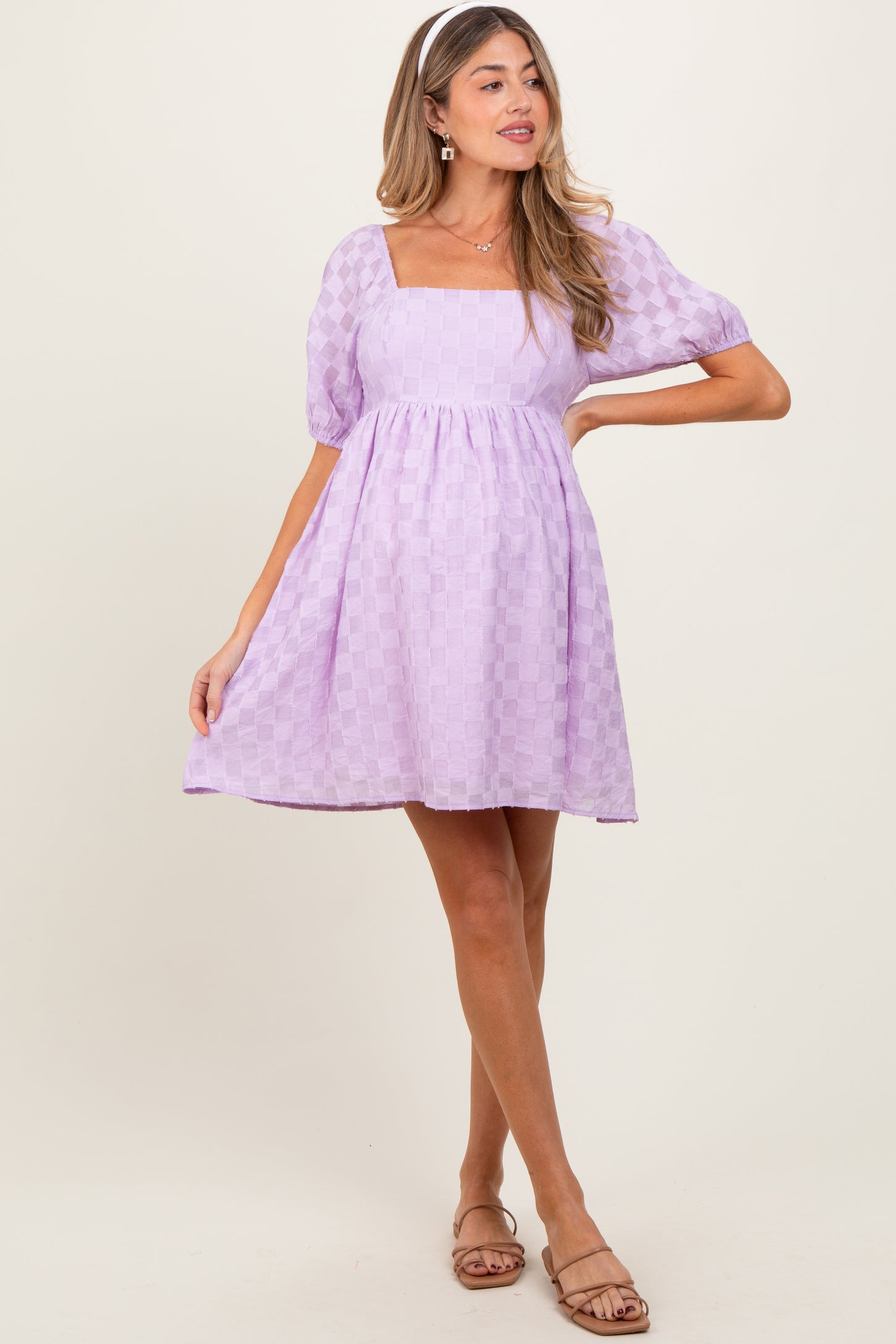 woman wearing a lavender maternity dress with a square neckline and puff sleeves, standing in a playful pose