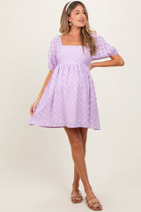 woman wearing a lavender maternity dress with a square neckline and puff sleeves, standing in a playful pose