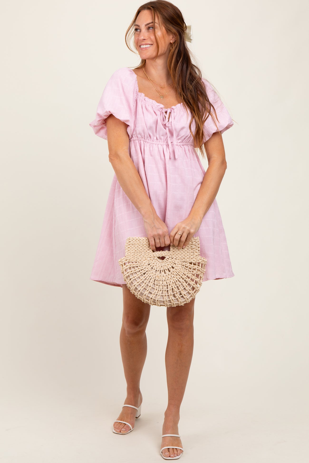 woman wearing a pink short puff sleeve dress and holding a circular straw handbag