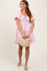 woman wearing a pink short puff sleeve dress and holding a circular straw handbag