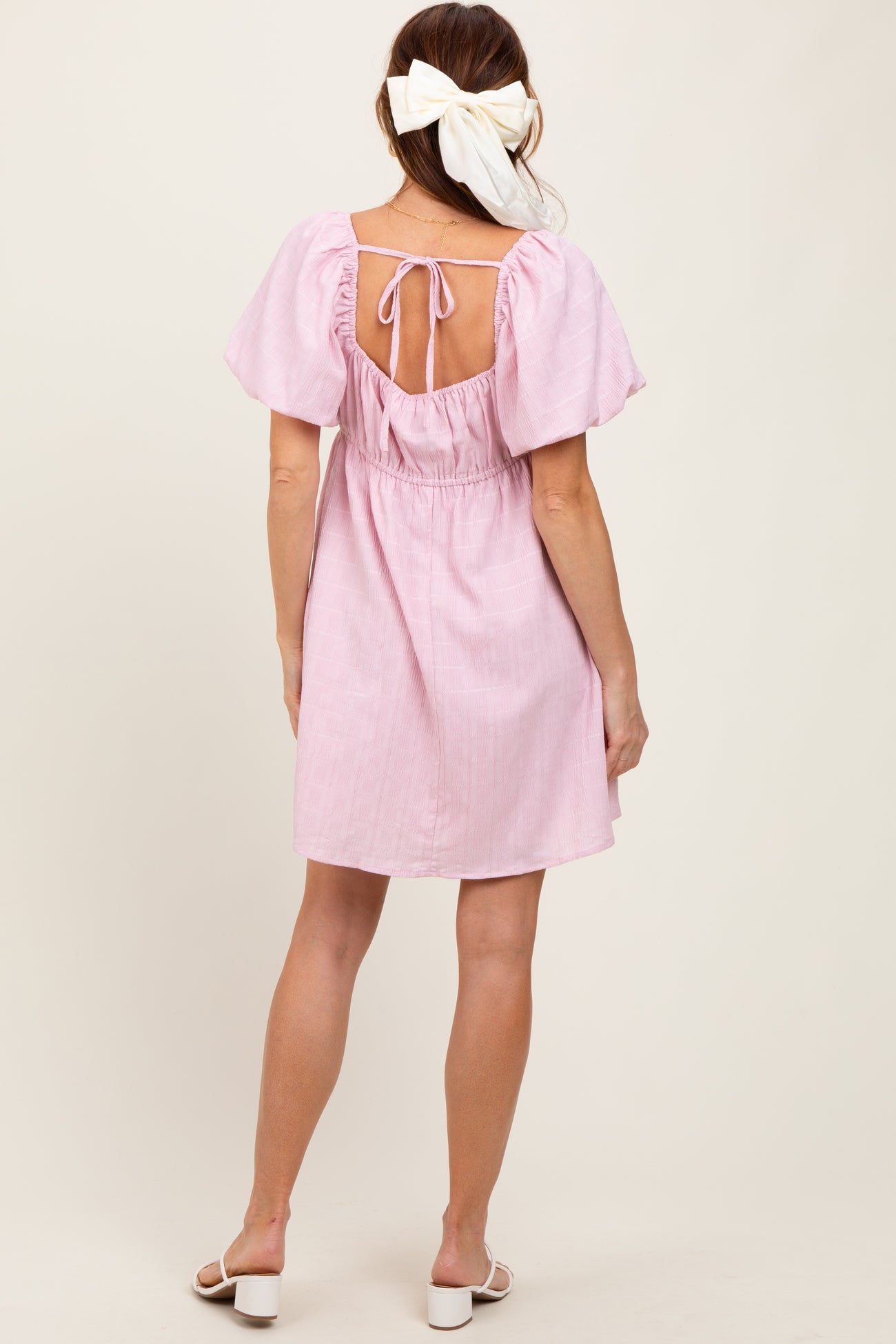 woman wearing a pink short sleeve dress with a tied back and a cinched waist, standing with her back to the camera