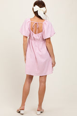 woman wearing a pink short sleeve dress with a tied back and a cinched waist, standing with her back to the camera