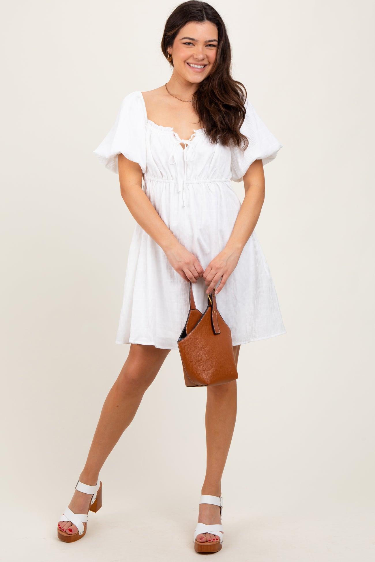 woman wearing a white short sleeve dress with a drawstring waist and holding a brown handbag