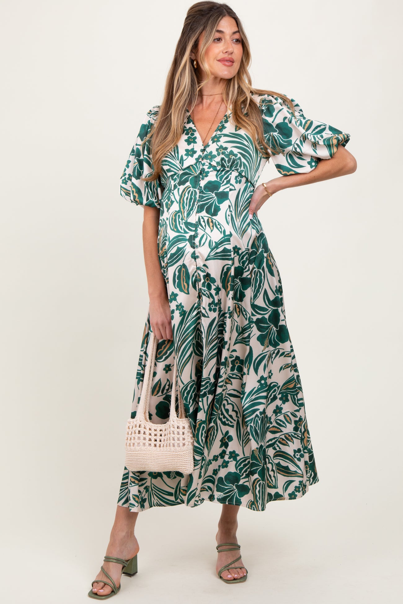 woman wearing a green and white floral maternity dress with puff sleeves and a tied waist, holding a woven bag