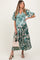 woman wearing a green and white floral maternity dress with puff sleeves and a tied waist, holding a woven bag