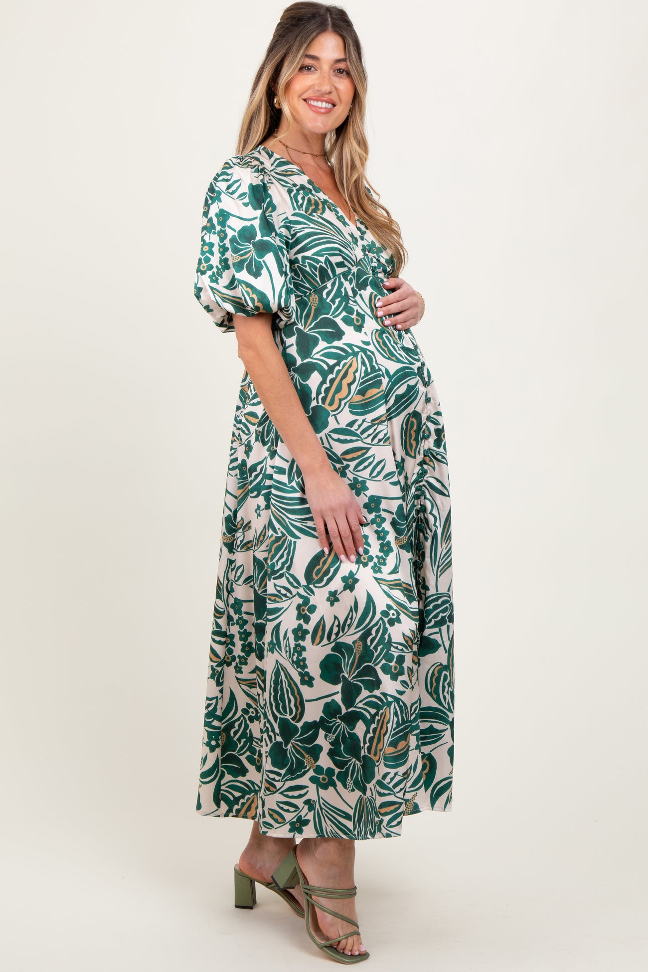 woman wearing a green floral print maternity dress with puff sleeves, cradling her baby bump