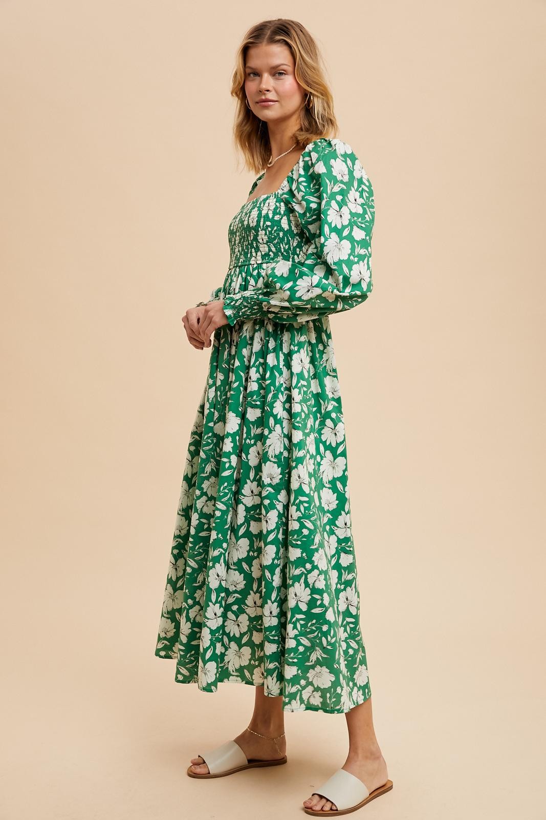 woman wearing a long green floral dress with puffed sleeves and a fitted bodice, standing on a neutral background