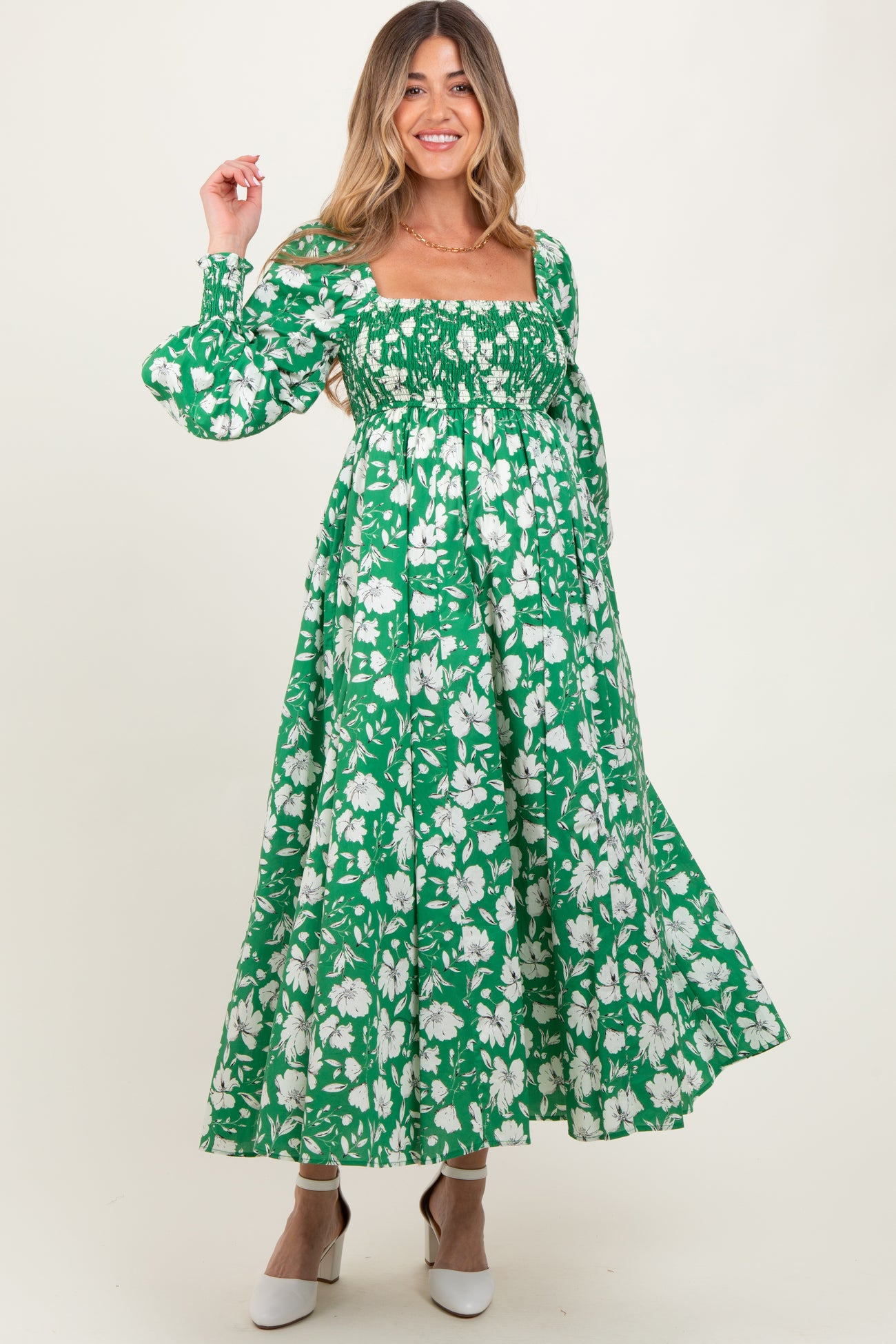 woman wearing a green floral maternity dress with puff sleeves and a smocked bodice, showcasing her baby bump