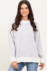 woman wearing a light gray ribbed pullover sweater with long sleeves and a relaxed fit, paired with blue jeans