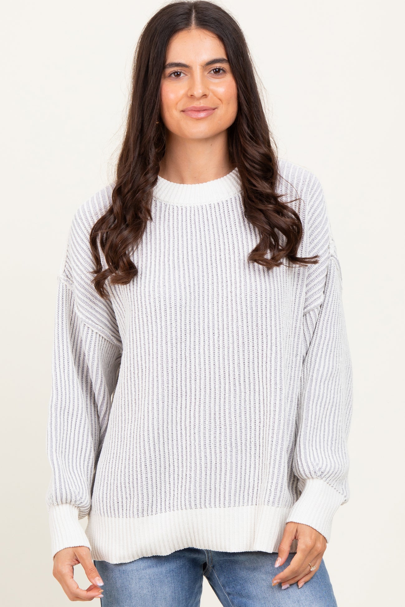 woman wearing a light gray striped oversized sweater with a ribbed texture and white cuffs