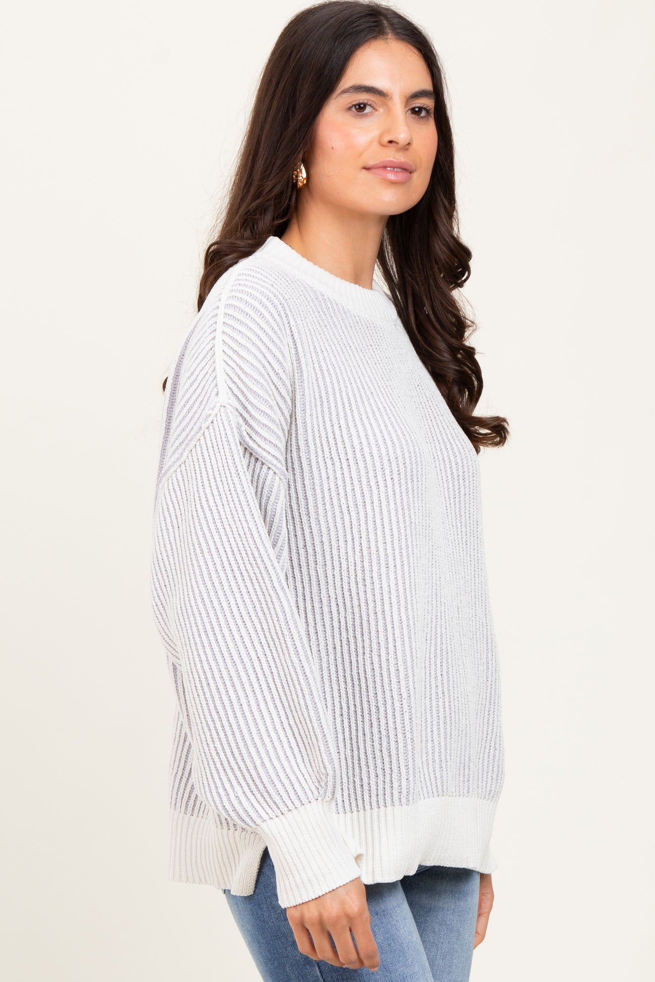 woman wearing a light gray oversized ribbed sweater with a white hem and cuffs, paired with blue jeans