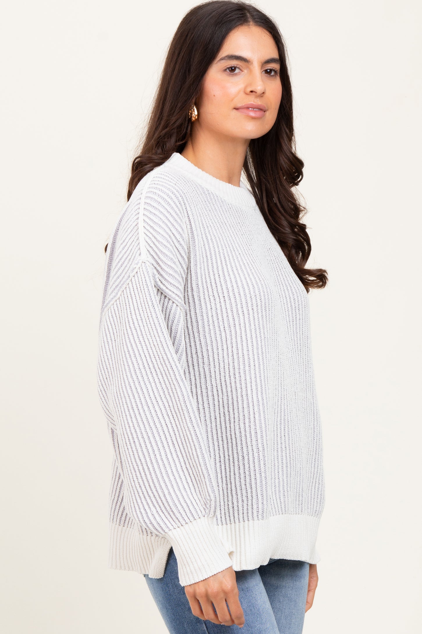 woman wearing a light gray oversized ribbed sweater with a white hem and cuffs, paired with blue jeans