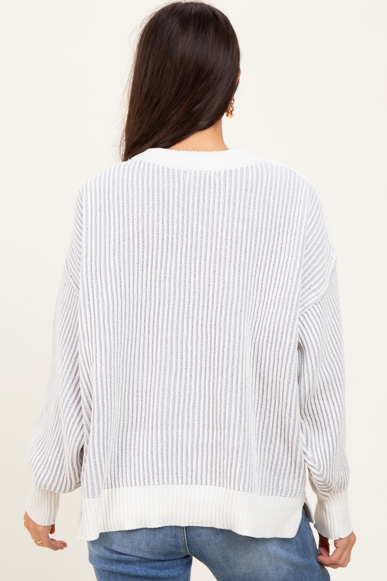 woman wearing a loose-fitting white striped sweater with long sleeves and a ribbed texture