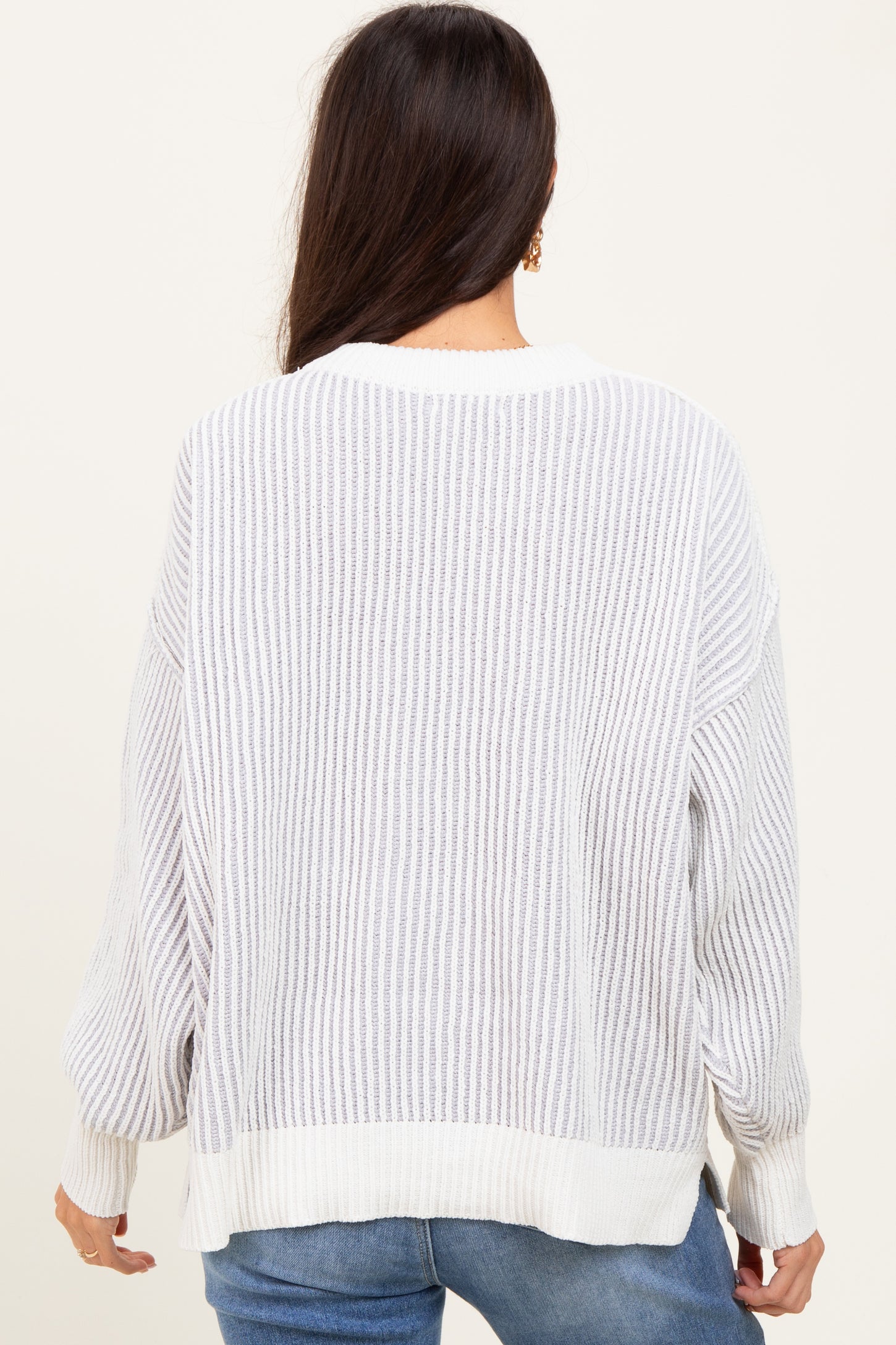 woman wearing a loose-fitting white striped sweater with long sleeves and a ribbed texture