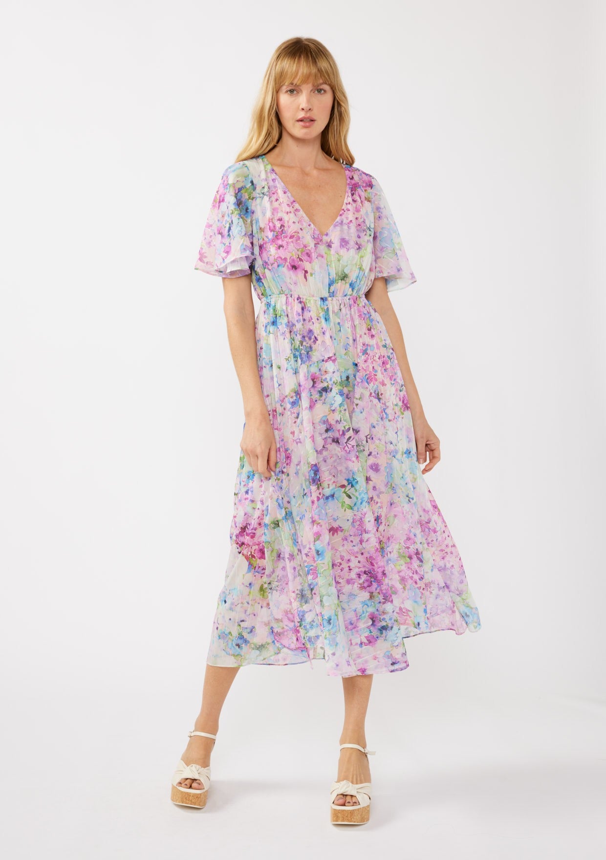 woman wearing a long, flowing floral maxi dress in pastel shades of purple, pink, and blue with short sleeves