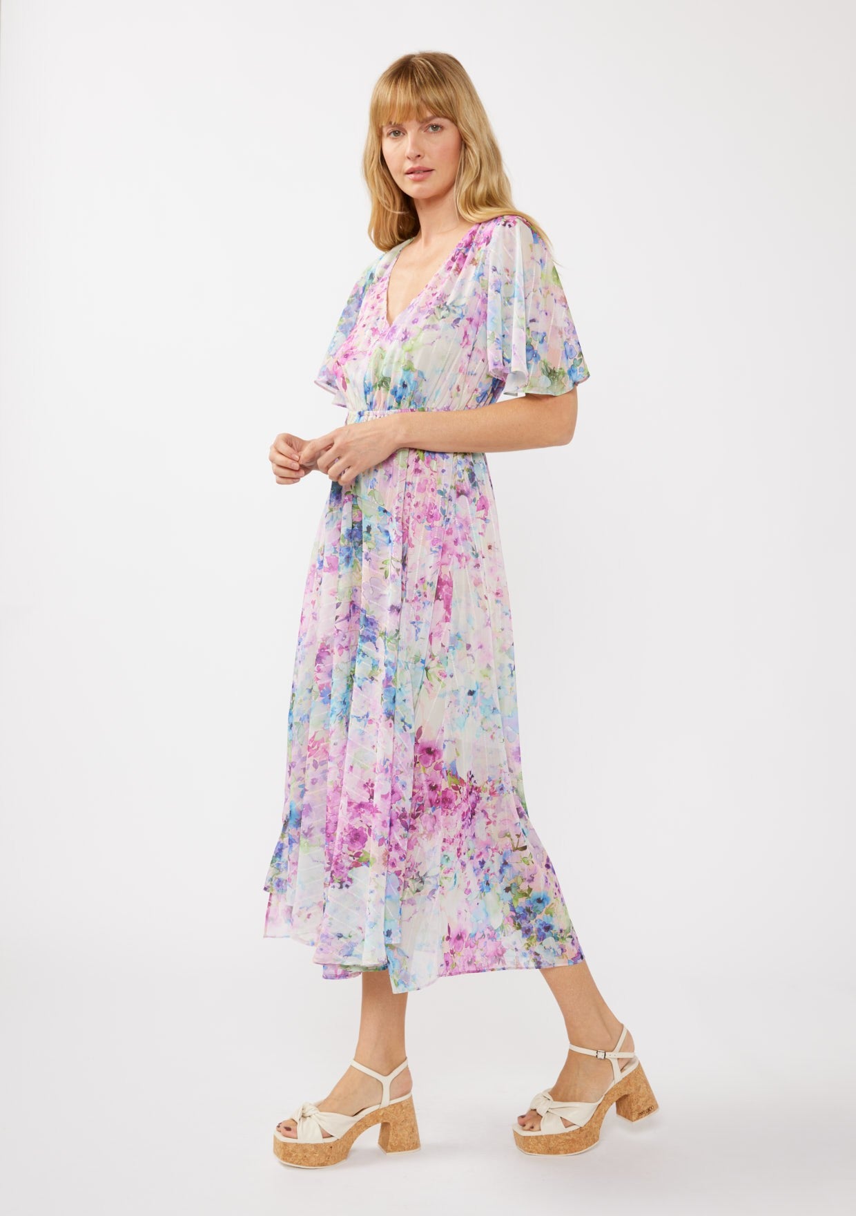 woman wearing a colorful floral maxi dress with short sleeves and a v-neckline, paired with platform sandals