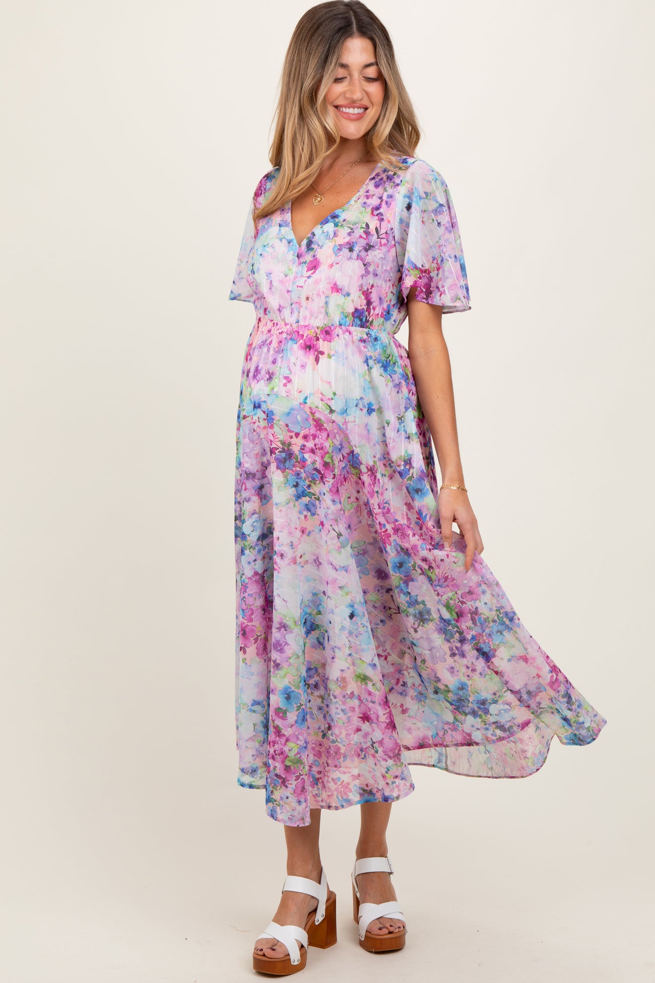 woman wearing a pastel floral print maternity dress with flutter sleeves and a flowy skirt, highlighting her baby bump