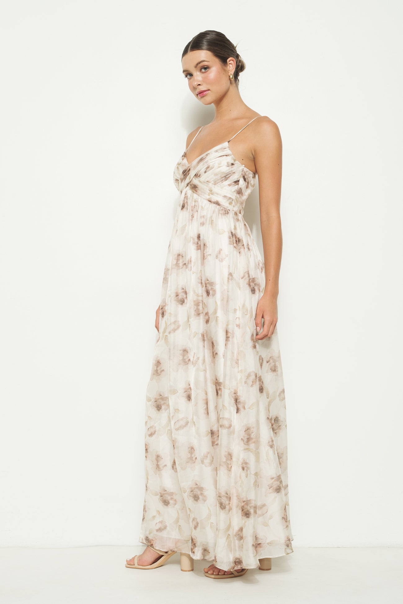 woman wearing a sleeveless maxi dress with a floral pattern in beige and brown tones, standing against a white background
