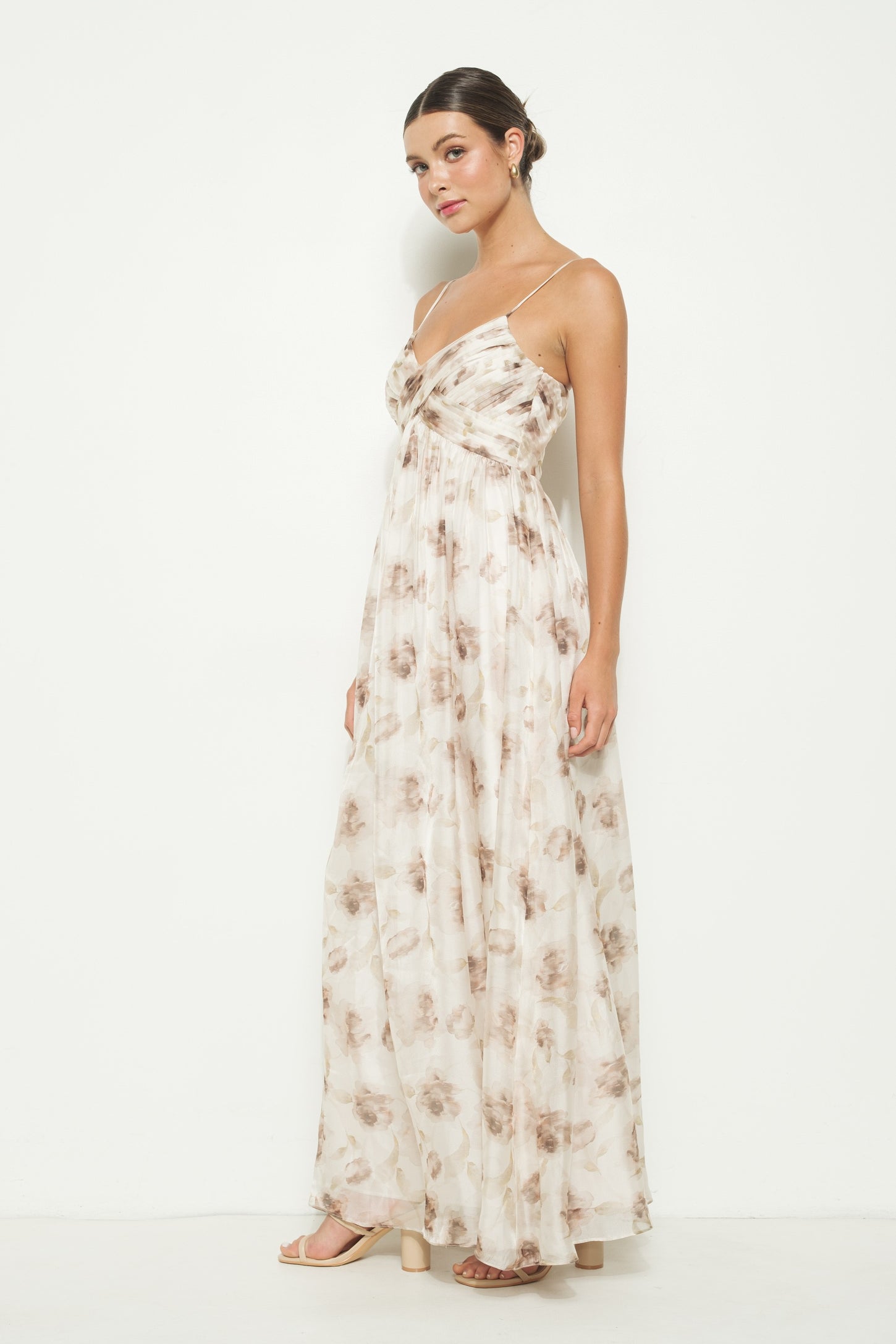 woman wearing a sleeveless maxi dress with a floral pattern in beige and brown tones, standing against a white background