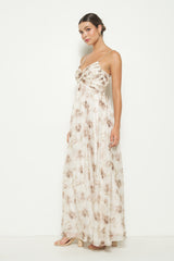 woman wearing a sleeveless maxi dress with a floral pattern in beige and brown tones, standing against a white background