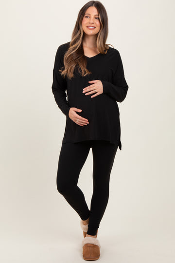 woman wearing a black long sleeve maternity top and black leggings, holding her baby bump