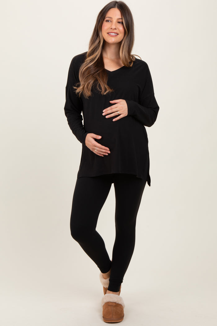 woman wearing a black long sleeve maternity top and black leggings, holding her baby bump