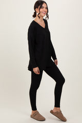 woman wearing a black long sleeve tunic top with side slits and black leggings, styled with beige slip-on shoes