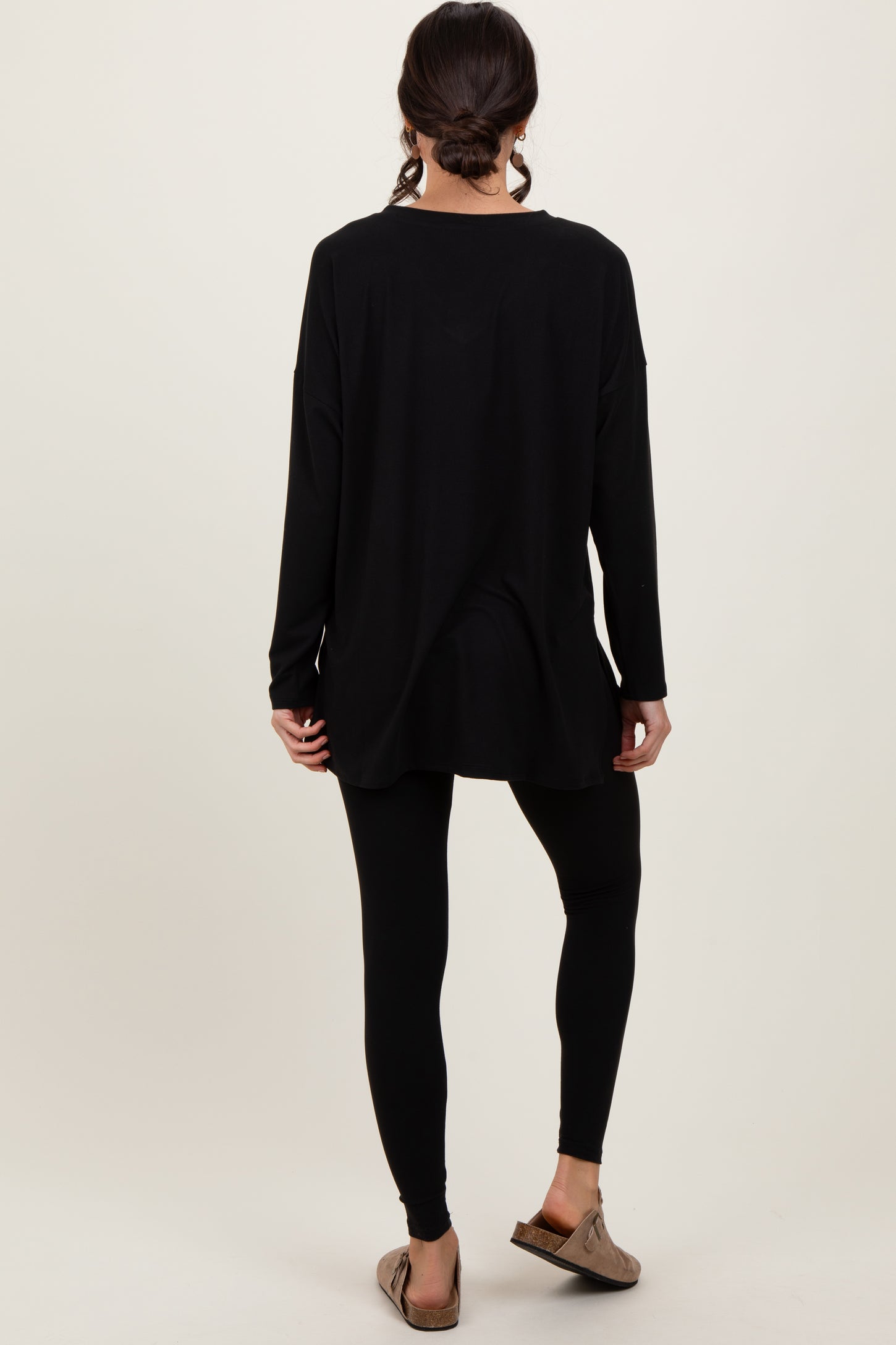 woman wearing a black long sleeve tunic top and black leggings, standing with back turned to the camera
